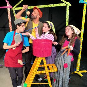 Four villagers stand around a small ladder with a bright pink soup bucket on top