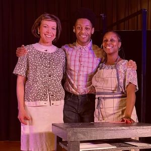 3 people stand together behind a small table, one white woman and two black people