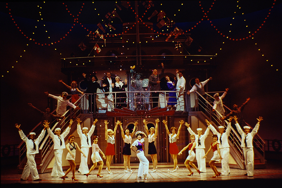 Anything Goes 2000s - sailors and cruise ship guests dancing on two levels of the ship's deck with arms outstretched