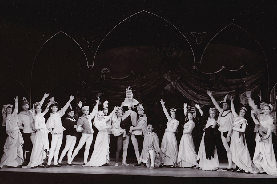 Once Upon a Mattress 60s - an ensemble of actors lining the front of the stage wearing medieval costumes. The princess is sitting on the shoulders of two gentlemen.